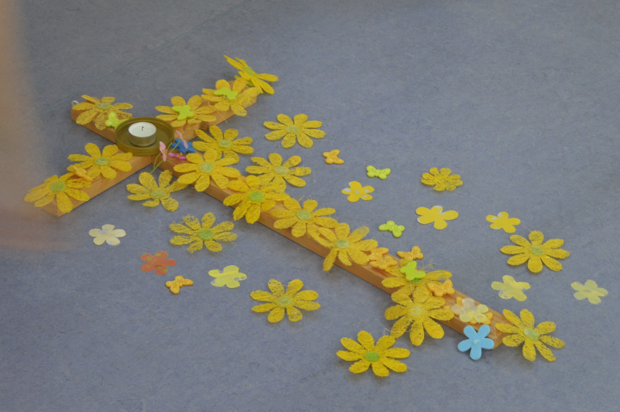 Holzkreuz mit vielen gelben Blumen von SchülerInnen bedeckt